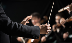 closeup of band conductors hands holding baton with band members in background out of focus