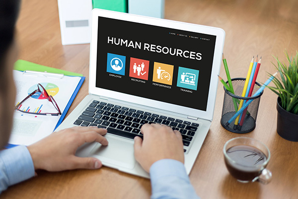 Closeup of a mans hands typing on computer with human resources on the screen and paperwork, a cup of coffee and pen holder with colored pencils