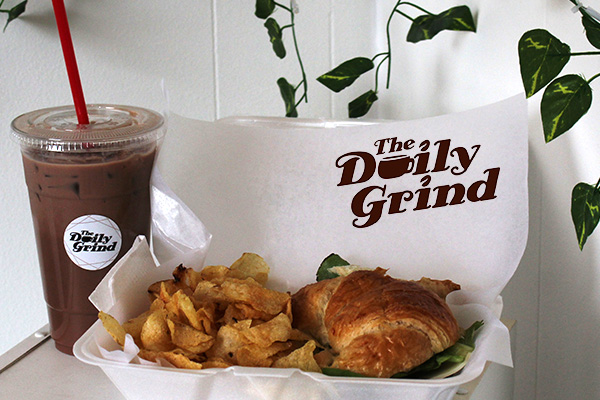 Cup of iced coffee next to deli sandwich on croissant with kettle chips in styrofoam to-go container